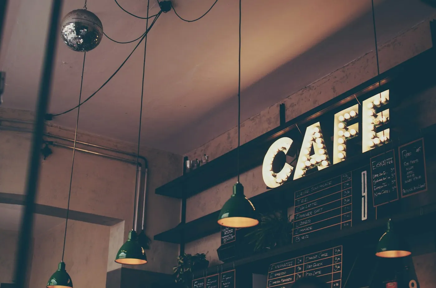 Interior de cafenea cu firma luminoasă CAFE pe perete și lămpi suspendate deasupra barului